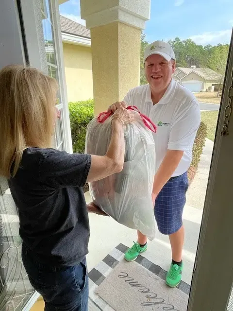 Chris Lenihan, owner of Dumpster Dash Valet, in branded uniform collecting trash at an apartment community at night with the company van in the background